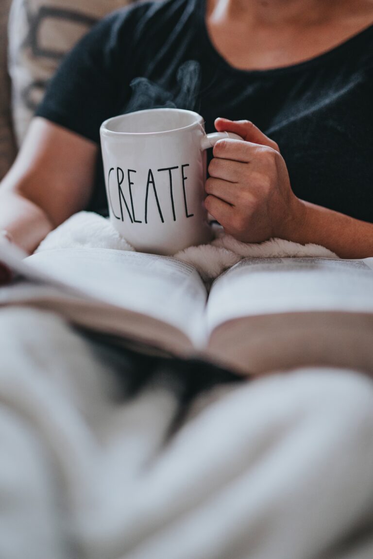 person in bed holding a create mug and reading a book