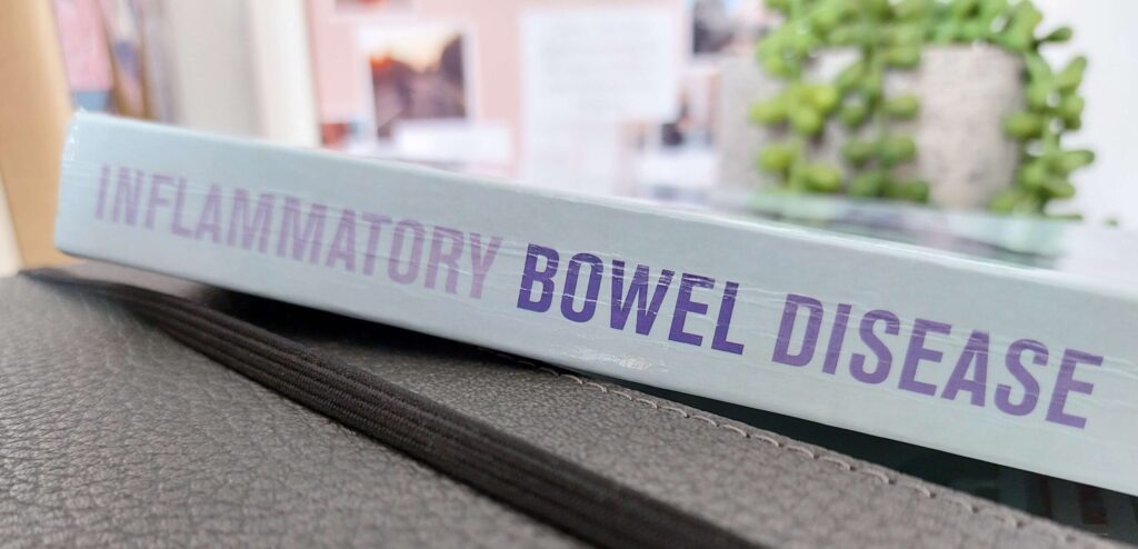 Pale blue book with title Inflammatory Bowel Disease resting on dark grey notebook to represent Working with IBD Hearth by Megan Elizabeth